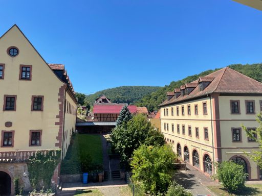 Blick auf historische Gebäude und grüne Hügel im Hintergrund unter klarem blauem Himmel.
