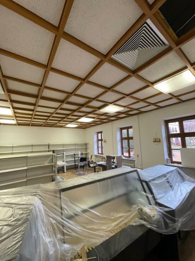 Leerer Raum mit Holzdecke, Regalen und abgedeckten Möbeln.